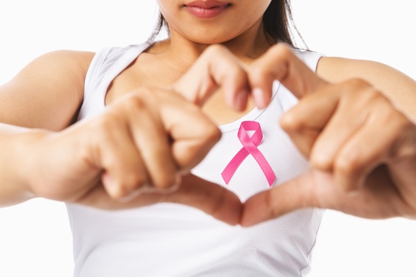 A woman makes a heart with her fingers over a pink ribbon to promote Breast Cancer Awareness